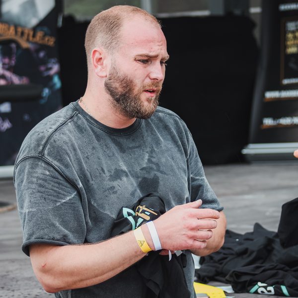 Barber s festivalovým páskem na ruce rozbaluje černá trička u stánku