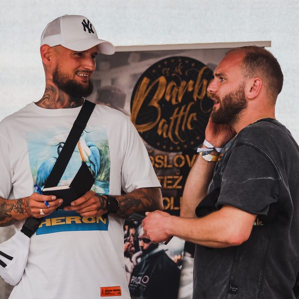 Dva barbeři se baví u banneru Barber Battle, jeden drží blok