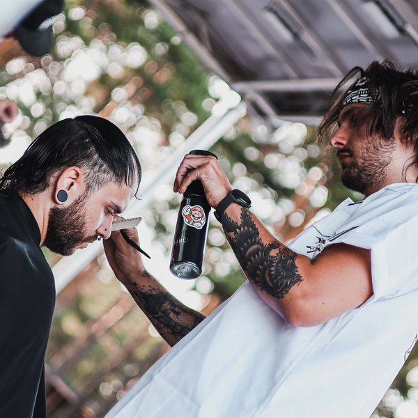 Barber s hřebenem v ústech pracuje s rozprašovačem na zákazníkovi v pláštěnce