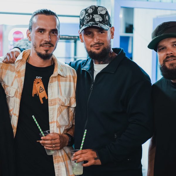 Tři barbeři s drinky v plastových kelímcích pózují u baru