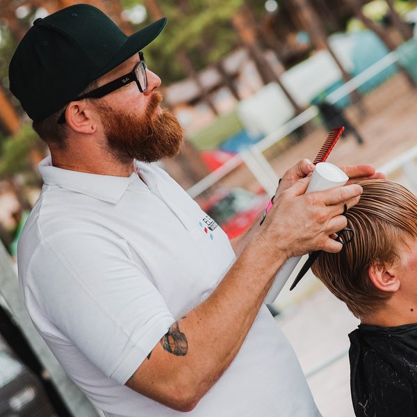 Barber s rezavým plnovousem češe červeným hřebenem vlasy zákazníka