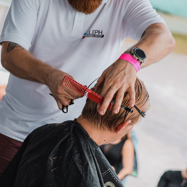 Detail rukou barbera stříhajících nůžkami přes červený hřeben