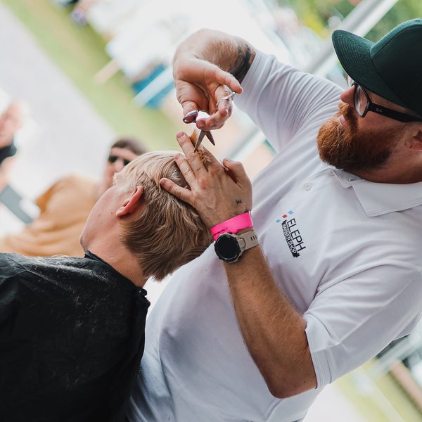 Barber v bílé polokošili zastřihuje nůžkami vlasy blond zákazníka