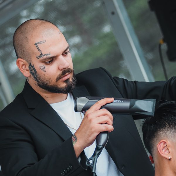 Barber v černém saku fénuje vlasy zákazníka na pódiu