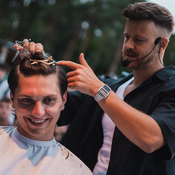 Lektor drží nůžky a ukazuje na sepnutý pramen vlasů modela