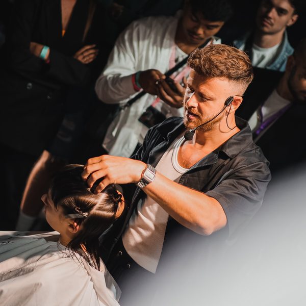 Lektor stříhá tmavovlasou modelku ve večerním světle, kolem stojí diváci