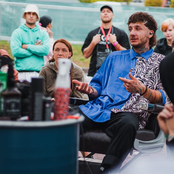 Lektor v modré košili mluví vsedě v barberském křesle před publikem
