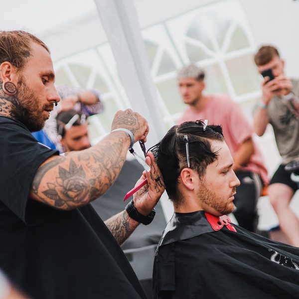 Barber s tunely v uších stříhá zákazníka, divák natáčí telefonem