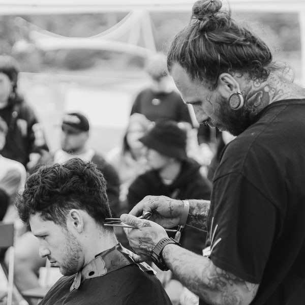 Barber s drdolem zastřihuje nůžkami kudrnaté vlasy zákazníka před diváky